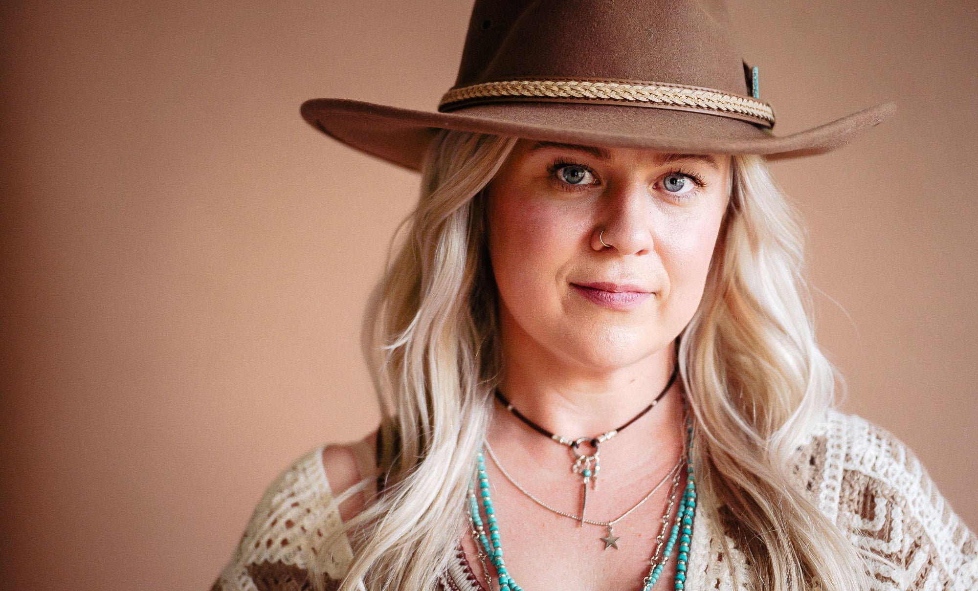 Woman wearing a brown hat and layered necklaces against a beige background