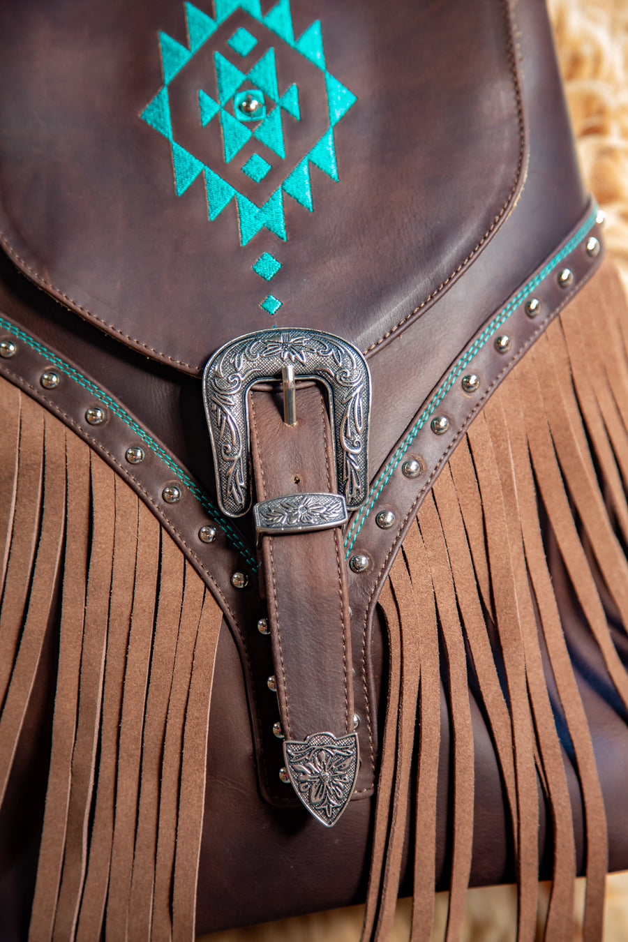 Brown leather saddle with turquoise embroidery and silver buckle on a blurred natural background