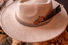 Beige cowboy hat with decorative band featuring a star and feather on a textured surface.