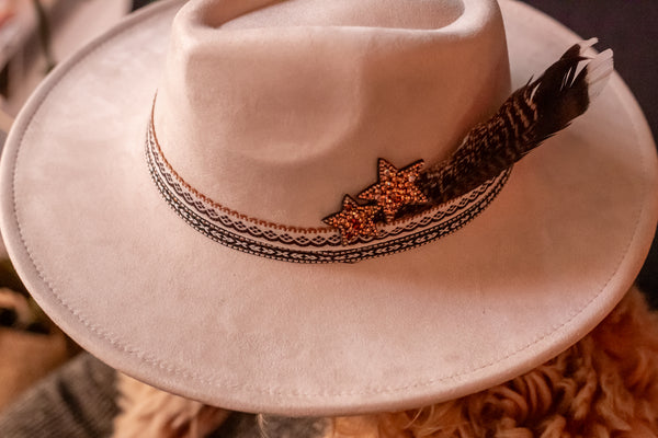 Beige cowboy hat with decorative band featuring a star and feather on a textured surface.