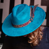 Turquoise hat with feather and patterned band on a dark background