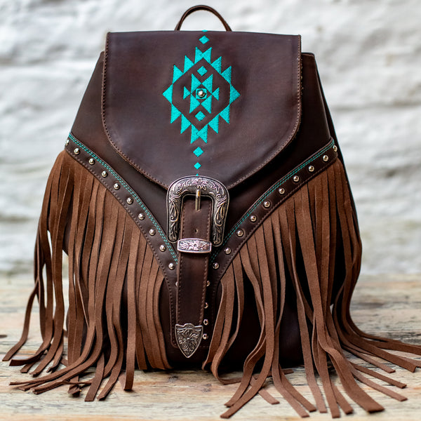 Brown leather backpack with turquoise geometric design and fringes on a wooden surface.