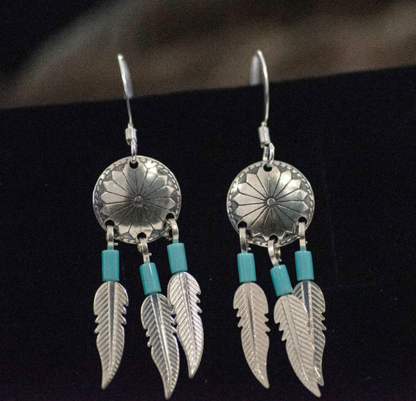 A classic Native American design. These earrings feature tripple dangling silver feathers  topped with Turquoise beads hanging from an intricate concho charm. The earrings are a hook style and are handmade by a Native American Artist. 